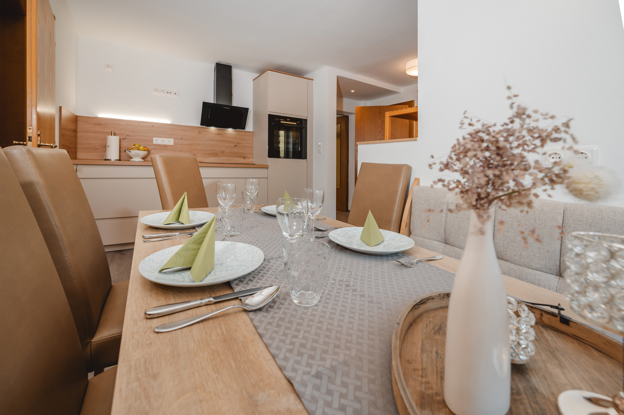 Monteur-Zimmer - Fernseher - Wagrain - Ein stilvoller Esstisch mit eleganten Platzgedecken und Besteck. Im Hintergrund ist eine moderne Küche zu sehen. Es gibt ein Induktionskochfeld, einen Backofen, sowie eine Mikrowelle.  - Haus Ortsblick