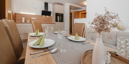 Monteur-Zimmer - Österreich - Ein stilvoller Esstisch mit eleganten Platzgedecken und Besteck. Im Hintergrund ist eine moderne Küche zu sehen. Es gibt ein Induktionskochfeld, einen Backofen, sowie eine Mikrowelle.  - Haus Ortsblick