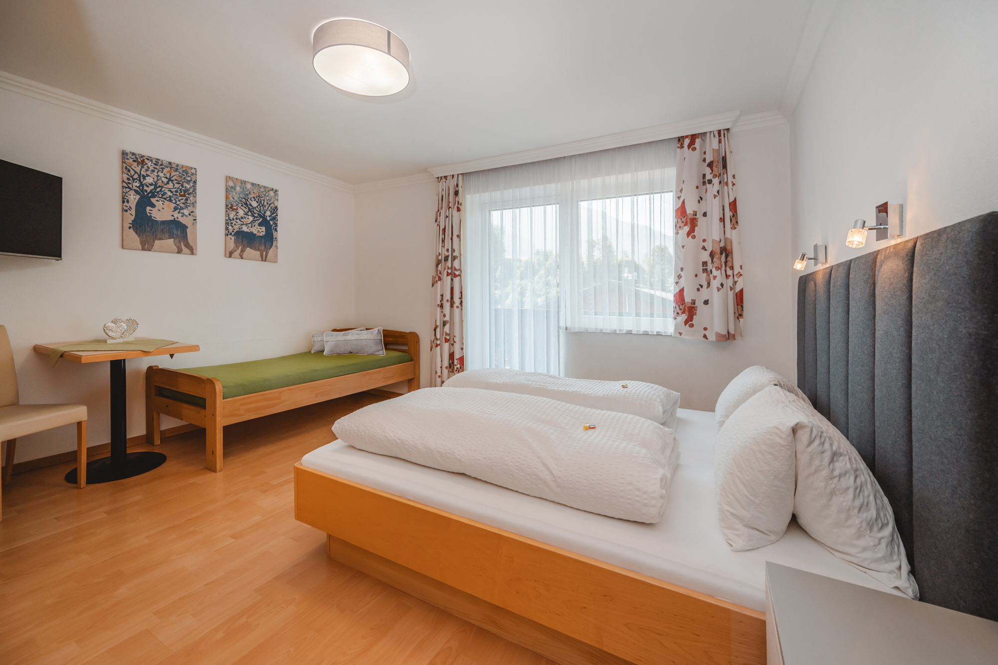 Monteur-Zimmer - Fernseher - Wagrain - Ein großes Schlafzimmer mit einem Doppelbett und einem zusätzlichen Einzelbett. Große Fenster sorgen für viel Tageslicht und eine freundliche Atmosphäre. Weiters ist ein Flat TV zu sehen. - Haus Ortsblick