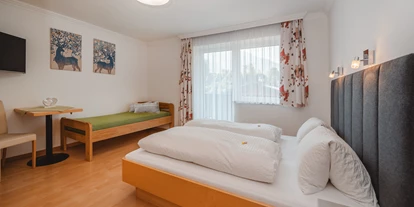 Monteur-Zimmer - Österreich - Ein großes Schlafzimmer mit einem Doppelbett und einem zusätzlichen Einzelbett. Große Fenster sorgen für viel Tageslicht und eine freundliche Atmosphäre. Weiters ist ein Flat TV zu sehen. - Haus Ortsblick