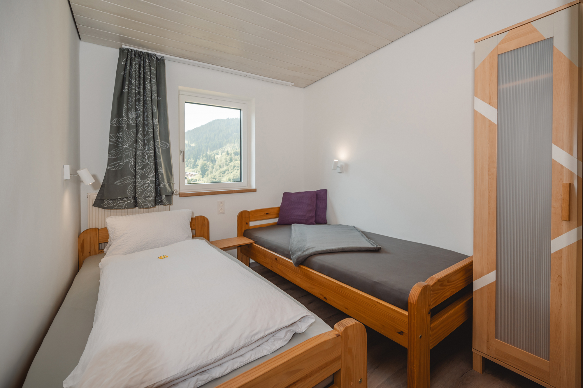 MonteurZimmer: Ein einfaches Schlafzimmer mit zwei Betten und einem Fenster. Die Wände sind hell und es gibt einen Schrank aus Holz. - Haus Ortsblick