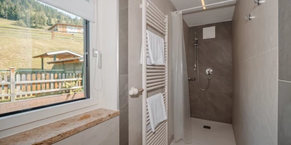 Monteur-Zimmer - Österreich - Ein modernes Badezimmer mit einer begehbaren Dusche und einem großen Fenster. Im Ausblick des Fensters sieht man eine grüne Landschaft mit einem Gartenhaus. - Haus Ortsblick
